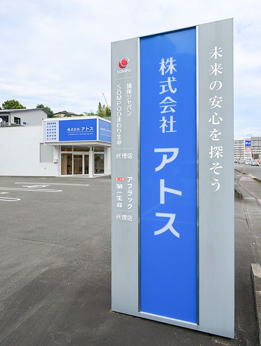 株式会社アトスの看板と背景に本社が写っている写真